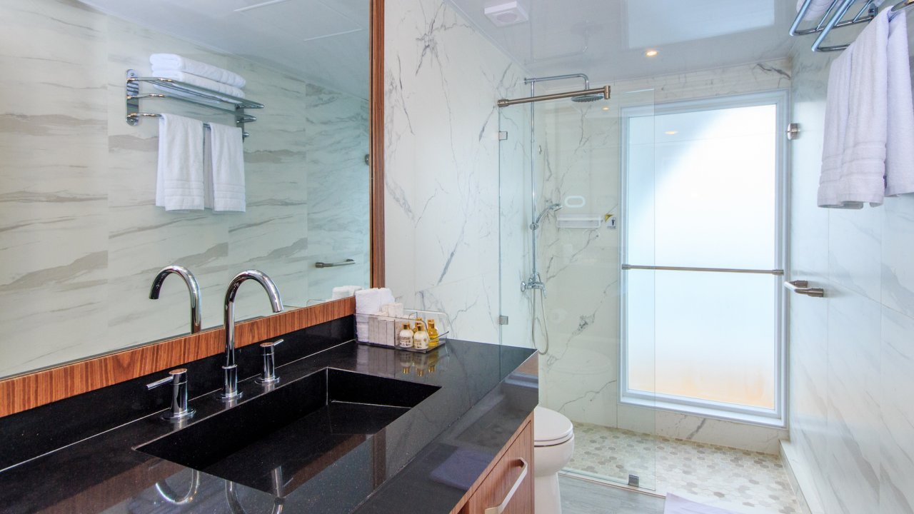 Modern bathroom with granite vanity and sink and tiled glass walk-in shower on a luxury yacht
