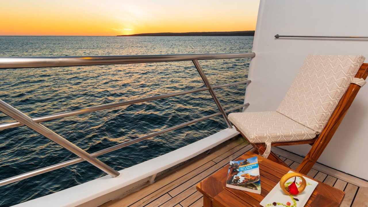 Empty chair next to a table with an appetizer on it on a small yacht cabin patio overlooking the water at sunset