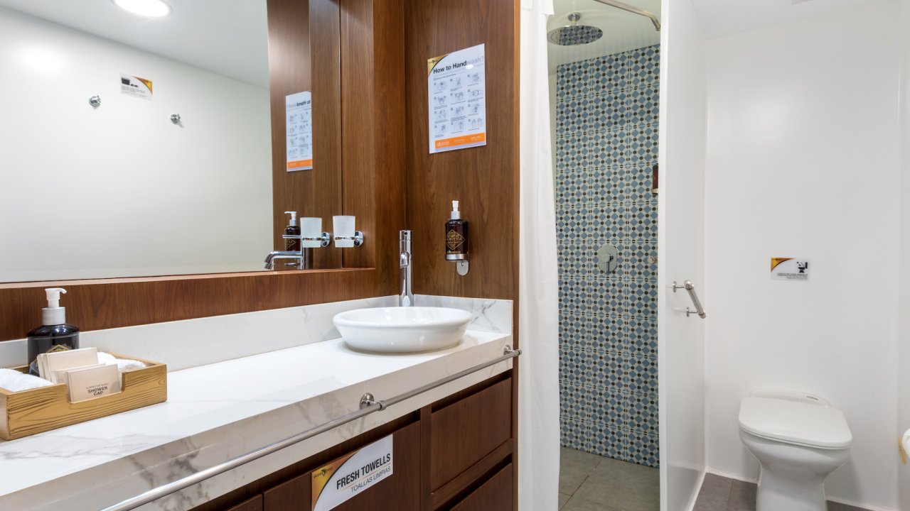 Bathroom sink and vanity with toilet and tiled shower in the background aboard a small luxury yacht