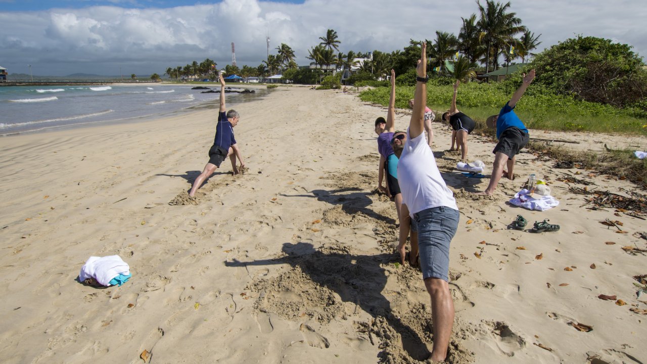 Group of people on a beach doing yoga with waves crashing in front of them in the Galapagos