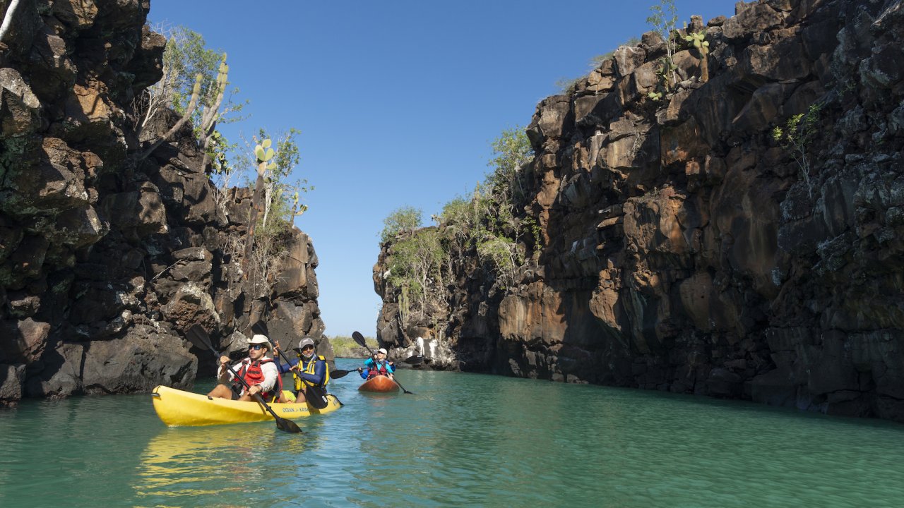 Two tandem kayaks with people paddling through a small channel in the Galapagos Islands