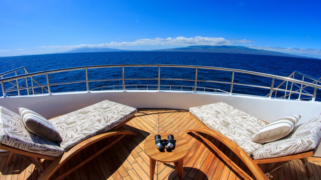 Two lounge chairs turned towards each other on the sky deck of a catamaran overlooking the Pacific Ocean on a sunny day