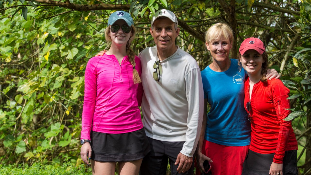 A family of mom, dad, and two daughter smiling in front of the lush forests of the Galapagos 