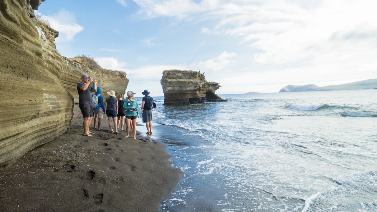 People standing on a black sand beach with rock formations behind them in the Galapagos