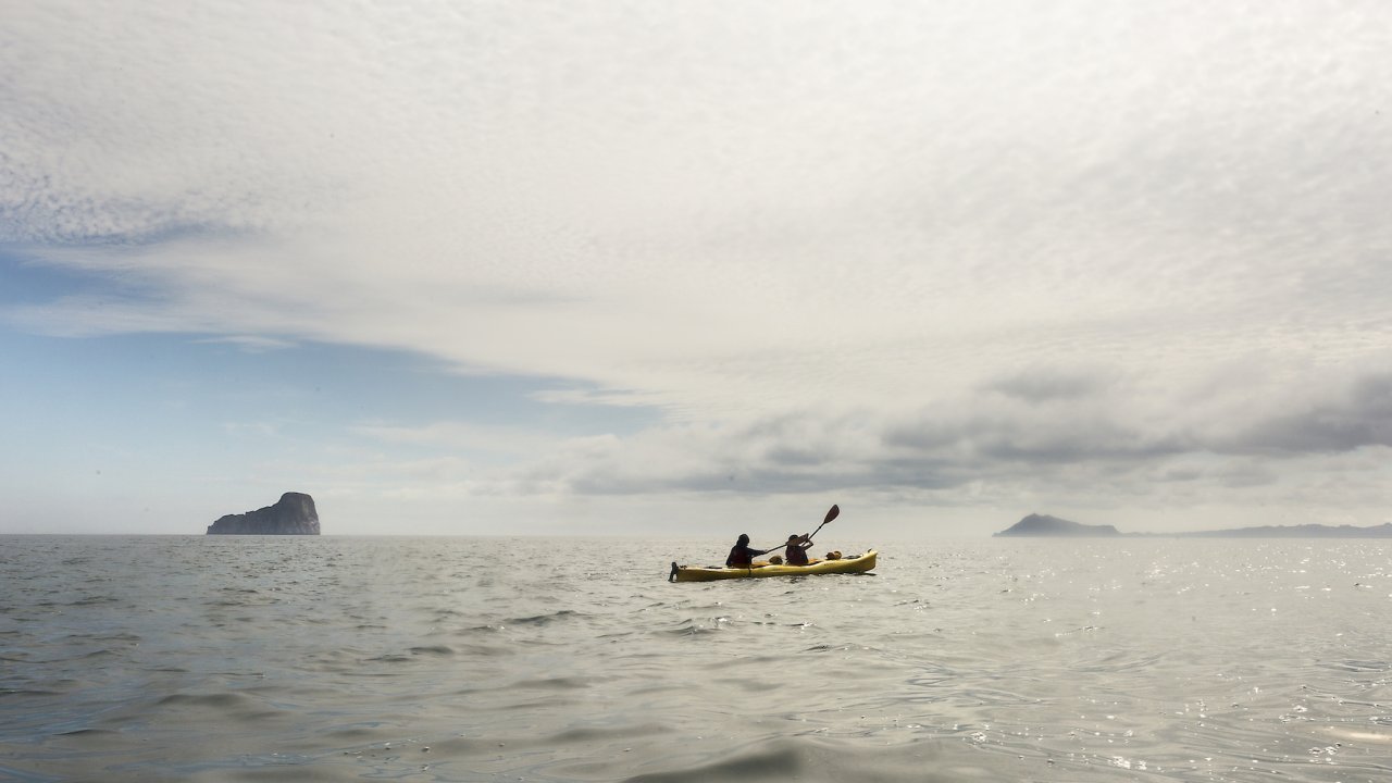 A yellow tandem kayak paddling by itself on the open ocean on a cloudy day in the Galapagos