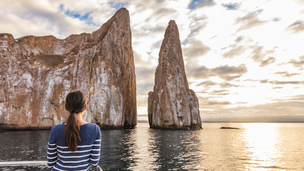 A woman looking out at Kicker Rock from the deck of a yacht at sunset in the Galapagos