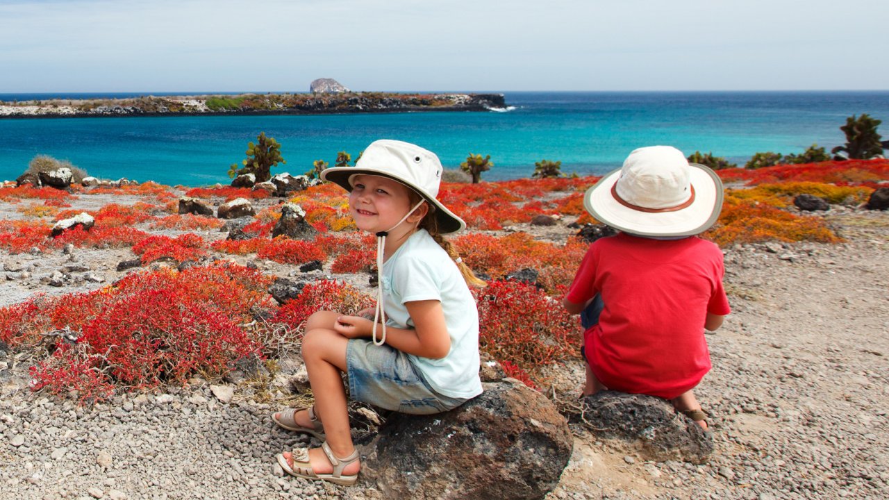 Two kids sitting on rocks on the beach enjoying the blue water in the Galapagos