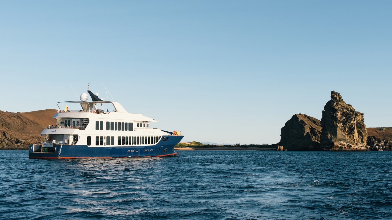 A small cruise ship passing by rocks jetting out of the Pacific Ocean in the Galapagos Islands