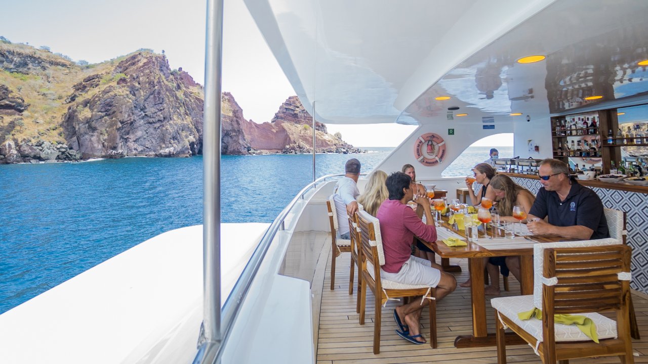 A group of people around a table on a sky deck of a small cruise ship in the Galapagos