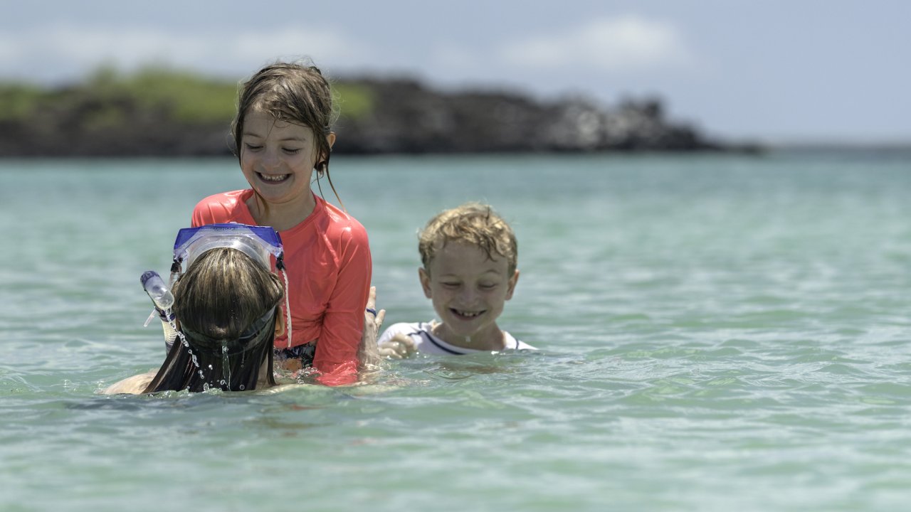 Two kids playing with their mom in the water while on vacation in the Galapagos