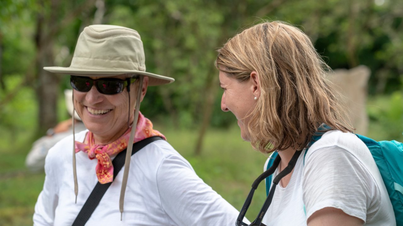 Close up of a woman smiling at a man with sunglasses and a hat while on a hike in the Galapagos
