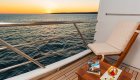 Empty chair next to a table with an appetizer on it on a small yacht cabin patio overlooking the water at sunset