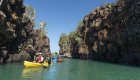 Two tandem kayaks with people paddling through a small channel in the Galapagos Islands