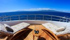 Two lounge chairs turned towards each other on the sky deck of a catamaran overlooking the Pacific Ocean on a sunny day