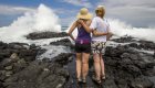 Mom and daughter with their hands behind each others backs looking over a wave crashed on the rocks they are standing on