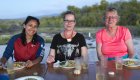 Three ladies on a beach eating dinner at a table while camping in the Galapagos