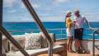 Couple both holding a glass of white wine wearing matching hats on the sundeck of a luxury cruise in the Galapagos Islands 