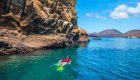A person snorkeling in blue green water next to rock formations on a sunny day in the Galapagos Islands