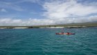 A red tandem kayak by itself paddling through the turquoise waters of the Galapagos Islands