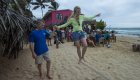 A girl walking across a slack-line while holding a mans hand for stability on a busy beach in the Galapagos
