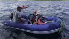 A family with a local guide riding an inflatable boat across blue waters on a Galapagos trip, with kayaks and lush islands in the background.
