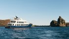 A small cruise ship passing by rocks jetting out of the Pacific Ocean in the Galapagos Islands
