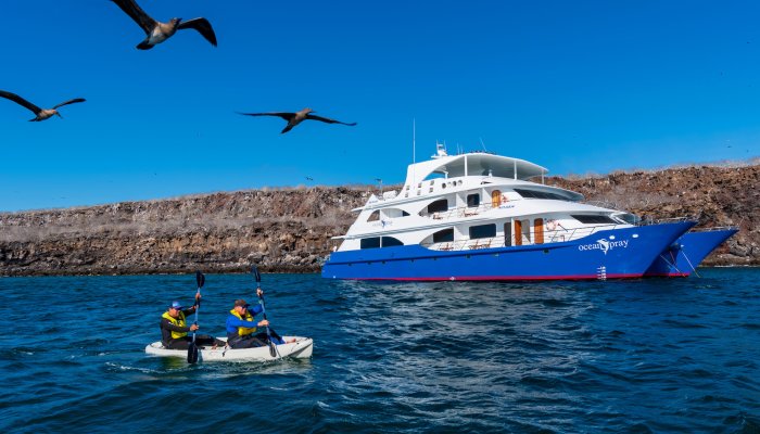 Tandem sea kayak with people paddling past the Ocean Spray small cruise ship in the Galapagos